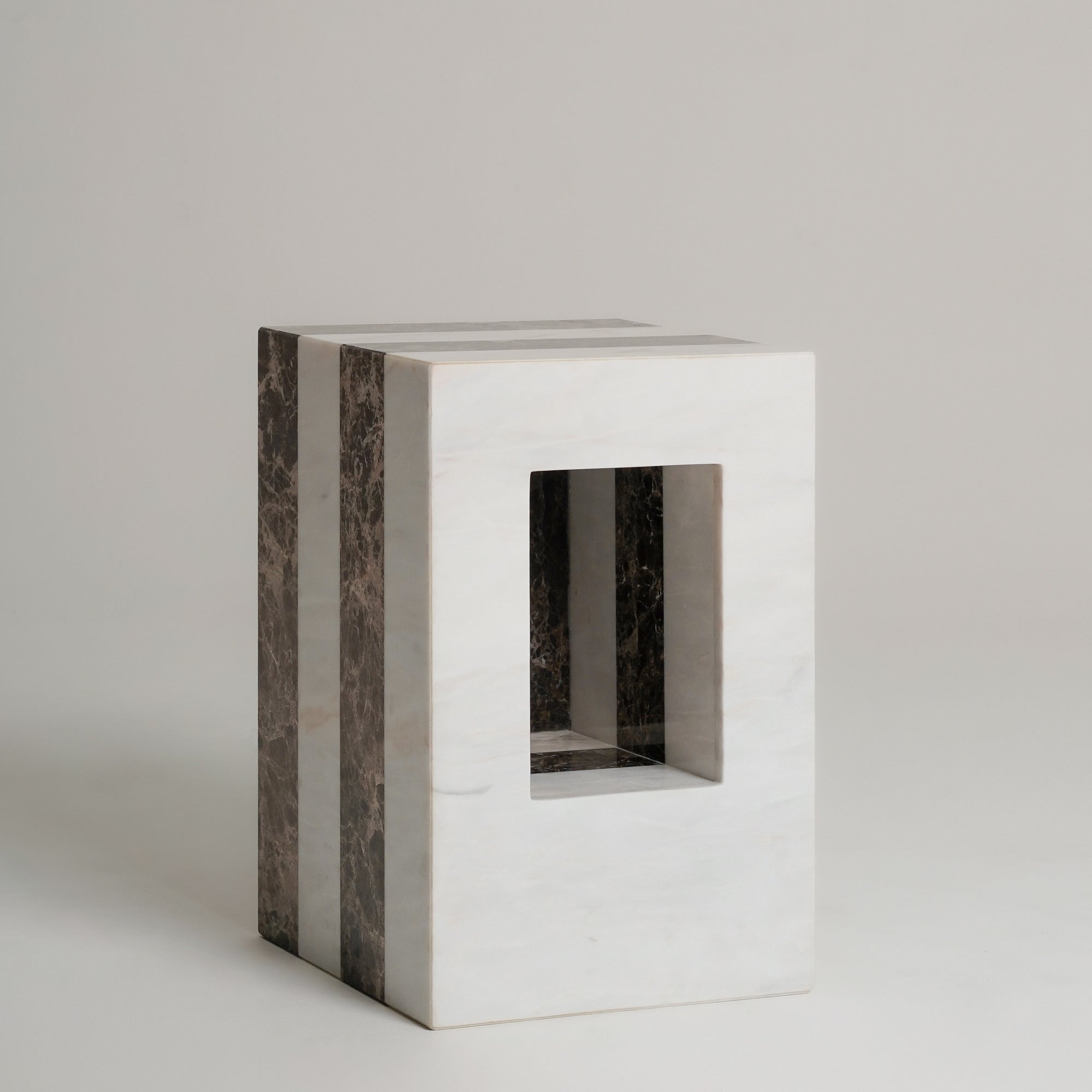 A timeless rectangular side table or stool made of white marble with dark brown veined side panels and a square cutout in the front, set against a neutral light gray background.