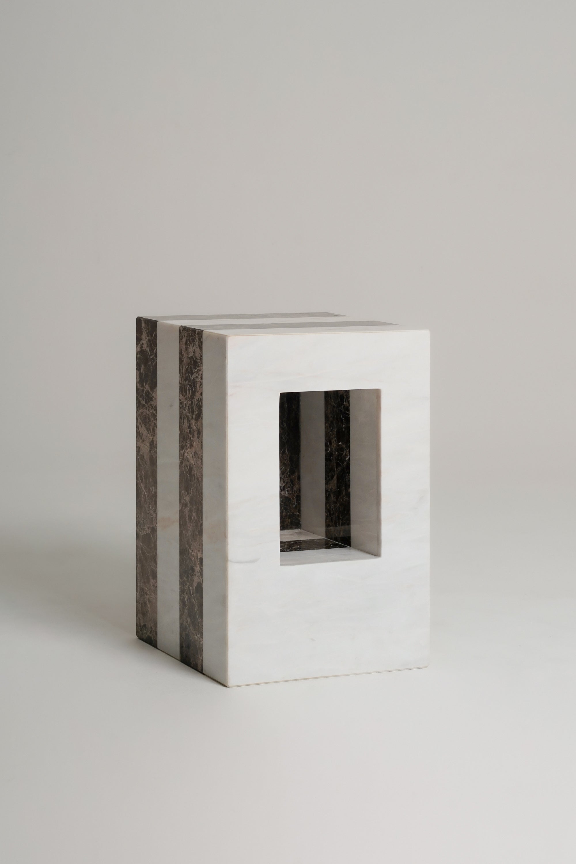 A timeless rectangular side table or stool made of white marble with dark brown veined side panels and a square cutout in the front, set against a neutral light gray background.