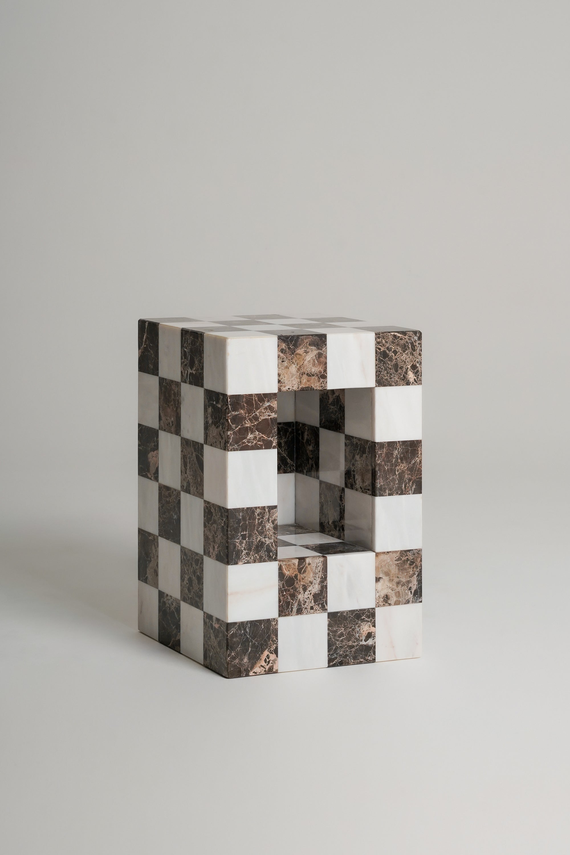 A small rectangular decorative object with a checkerboard pattern of white and dark brown marble tiles, featuring an open center, set against a plain light gray background.