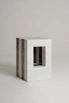 A timeless rectangular side table or stool made of white marble with dark brown veined side panels and a square cutout in the front, set against a neutral light gray background.