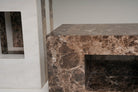 A close-up of two modern side tables from the stine series 02 made from dark brown marble with natural veining, featuring a rectangular open shelf and a thick top surface. 