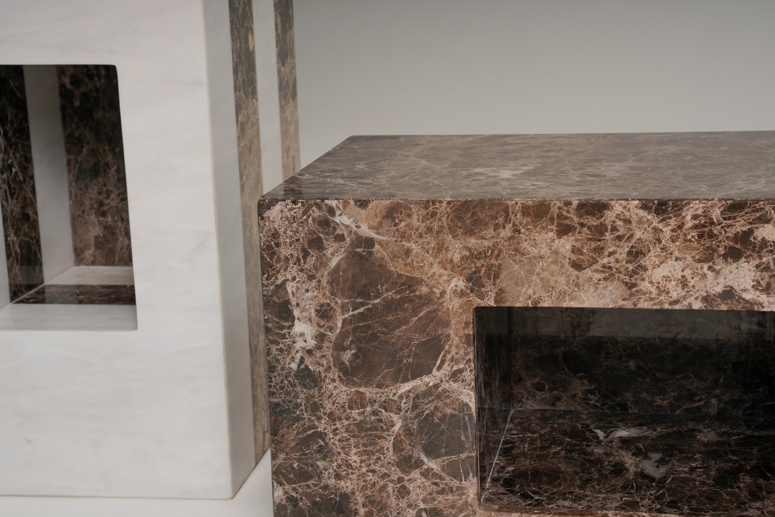 A close-up of two modern side tables from the stine series 02 made from dark brown marble with natural veining, featuring a rectangular open shelf and a thick top surface. 