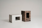 Two modernist stone block stools made of white and dark brown marble, shown on a seamless light gray studio background. 
