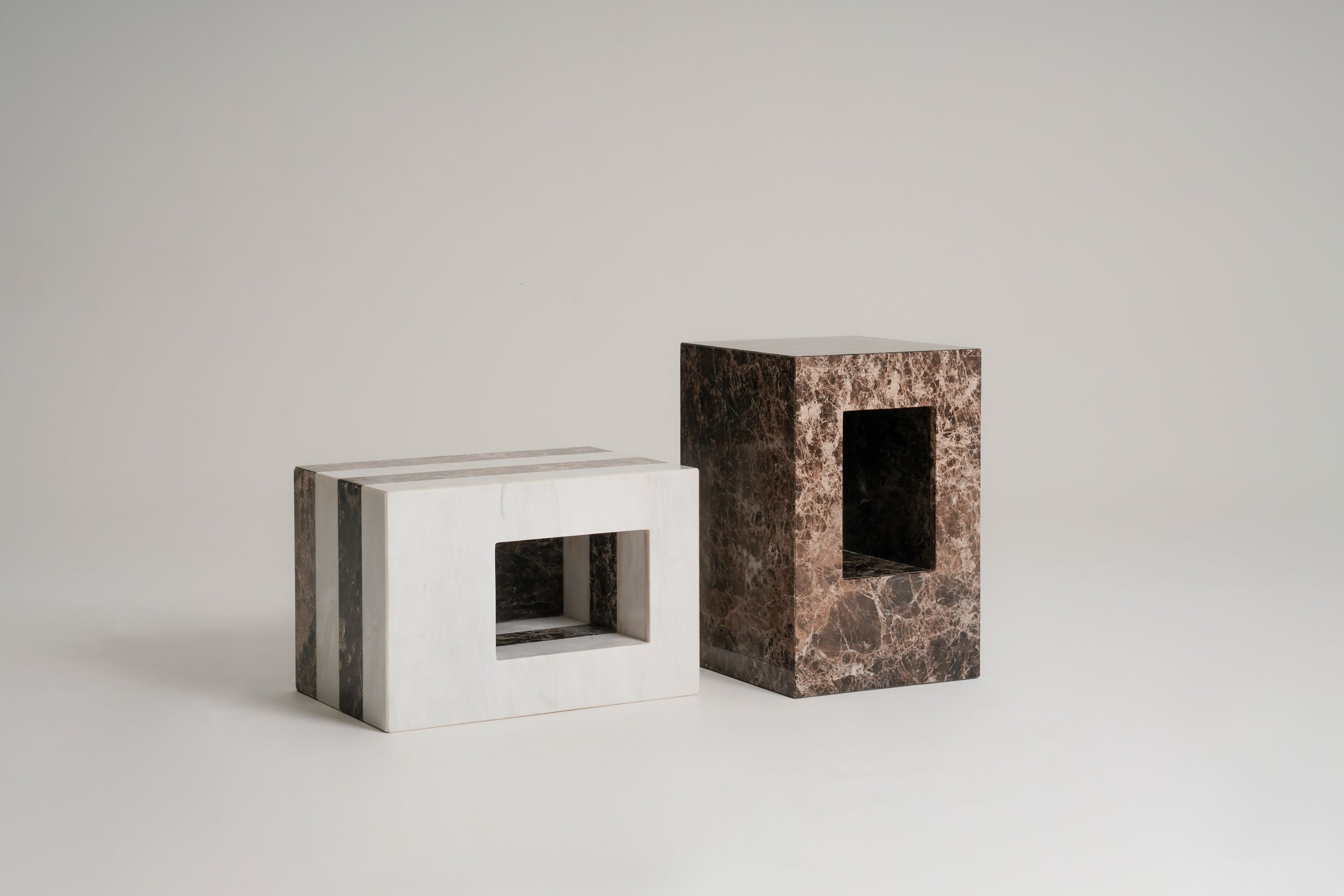 Two marble objects/stools made of white and dark brown marble, shown on a seamless light gray studio background.